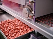 Современная фармацевтическая машина с грудами розовых таблеток на конвейере размещена в производственной лаборатории — стоковое фото