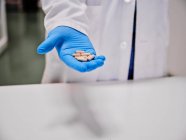 Анонимный ученый в защитных перчатках, стоящий с грудой капсул в лаборатории — стоковое фото