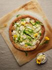 Draufsicht auf leckere Pizza mit Kürbisscheiben und Gewürzen mit frischen Rucolablättern auf Pergamentpapier auf beigem Hintergrund — Stockfoto