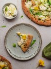 Вид сверху на аппетитный ломтик пиццы с листьями рукколы и цветок сквоша на расплавленном сыре на сером фоне — стоковое фото