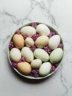 Вид сверху на сырые куриные яйца на круглой пластине с цветущими цветами лаванды на мраморной поверхности — стоковое фото