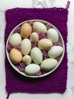 Вид зверху сирих курячих яєць на круглій тарілці з квітучими квітами Лавандули на фіолетовій серветці та мармуровій поверхні — стокове фото