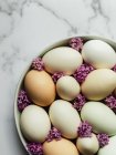 Вид зверху сирих курячих яєць на круглій тарілці з квітучими квітами Лавандули на мармуровій поверхні — стокове фото