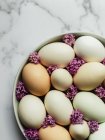 Overhead view of raw chicken eggs on round shaped plate with blossoming Lavandula flowers on marble surface — Stock Photo