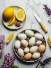 Vista dall'alto delle uova di pollo sul piatto tra fiori di Lavandula in fiore e fette di limone fresco con coltello — Foto stock
