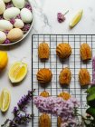 Vista dall'alto di gustose madeleine su scaffale di raffreddamento vicino al piatto con uova e fiori di lavanda sulla superficie di marmo — Foto stock