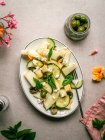Vue de dessus de délicieuse salade de melon avec des concombres et des olives servis dans une assiette avec des herbes près de salière et serviette — Photo de stock