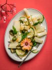 Верхний вид на вкусный салат из дыни с огурцами и оливками подается на тарелке с травами рядом с солонкой и салфеткой на красном фоне — стоковое фото