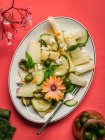 Vista superior de deliciosa ensalada de melón con pepinos y aceitunas servidas en plato con hierbas cerca de salero y servilleta sobre fondo rojo - foto de stock