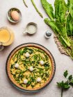 Vista dall'alto della deliziosa quiche cruda con prezzemolo posto vicino all'uovo e spinaci freschi con asparagi in tavola — Foto stock