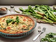 Yummy quiche with parsley placed near egg and fresh spinach with asparagus on table — Stock Photo