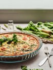 Leckere Quiche mit Petersilie neben Ei und frischem Spinat mit Spargel auf dem Tisch — Stockfoto