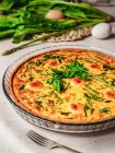 Yummy quiche with parsley placed near egg and fresh spinach with asparagus on table — Stock Photo