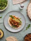 Top view of tortillas with fried tofu cubes and avocado pieces with fresh arugula leaves on tablecloth — Stock Photo