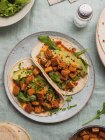 Top view of tortillas with fried tofu cubes and avocado pieces with fresh arugula leaves on tablecloth — Stock Photo