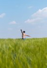 Rückenansicht eines Mannes mit nacktem Oberkörper in Jeans, der die Arme ausbreitet, während er im hohen Gras des ländlichen Feldes vorwärts läuft — Stockfoto