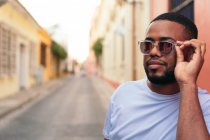 Homem afro-americano com óculos de sol andando na rua da cidade olhando para a câmera. — Fotografia de Stock