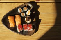 De cima prato com rolos de sushi variados servido em mesa de madeira no restaurante japonês — Fotografia de Stock