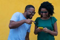 Couple noir à l'aide d'un téléphone portable appuyé contre un mur jaune — Photo de stock