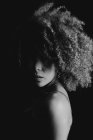 Black and white charming African American female model with curly hair looking at camera in dark studio — Stock Photo