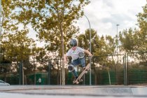 Adolescente saltando con monopatín y mostrando truco en rampa en skate park - foto de stock