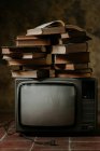 Mucchio di libri posti in cima alla TV d'epoca sul pavimento di piastrelle squallido — Foto stock