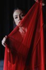 Cortar jovem fêmea com lábios vermelhos olhando para a câmera atrás de têxteis transparentes com pregas — Fotografia de Stock
