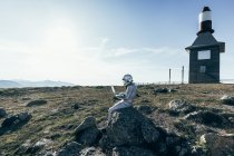 Homem astronauta de corpo inteiro em trajes espaciais navegando dados no netbook enquanto sentado na rocha fora da estação com antenas em forma de foguete — Fotografia de Stock