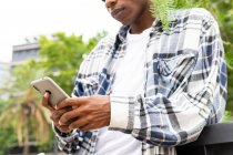 Desde abajo cogió mensajes masculinos afroamericanos irreconocibles en el teléfono móvil mientras estaba de pie en la calle de la ciudad - foto de stock