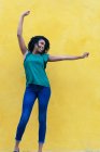 Laughing young African woman in front of yellow wall with raised arms — Stock Photo