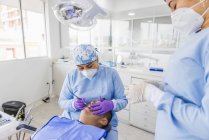 Жіночий стоматолог в уніформі та дихальній масці для лікування зубів пацієнта чоловічої статі в лікарні — стокове фото