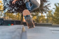 Cortar adolescente saltando com skate e mostrando acrobacia na rampa no parque de skate — Fotografia de Stock