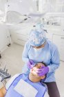 Von oben von einer anonymen Ärztin in Uniform, die Zähne eines männlichen Patienten mit Zahnretraktor im Krankenhaus reinigt — Stockfoto
