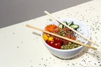 From above bamboo chopsticks placed on top of bowl with tasty poke dish on table covered with sesame seeds — Stock Photo