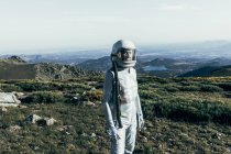 Astronauta masculino em trajes espaciais e capacete em pé na grama e pedras em terras altas — Fotografia de Stock