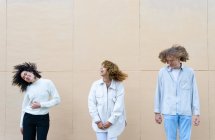 Група молодих різноманітних жінок і чоловік з кучерявим волоссям, що стоїть в ряд проти бежевої стіни розважається — стокове фото