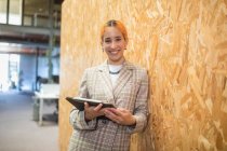 Smiling female entrepreneur standing with computer near wall in coworking space while looking at camera — Stock Photo