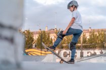 Vista laterale a basso angolo di coraggioso pattinatore adolescente in piedi sullo skateboard e che si prepara per mostrare trucco sulla rampa nello skate park — Foto stock