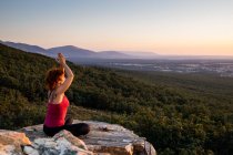 Joven yogi practicando yoga sobre una roca en la montaña con la luz del amanecer - foto de stock