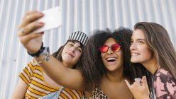 Três mulheres jovens bonitas de raças diferentes com suas pranchas longas tirando uma selfie com seu telefone inteligente — Fotografia de Stock