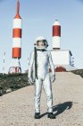 Mann im Raumanzug steht an sonnigen Tagen auf felsigem Boden gegen gestreifte raketenförmige Antennen — Stockfoto