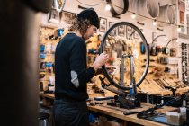 Вид сбоку молодого мастера, осматривающего колесо велосипеда во время работы в мастерской профессионального ремонта — стоковое фото