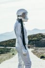 Вид сбоку на человека в скафандре и шлеме, который смотрит в сторону, стоя на дорожке в солнечный день на природе — стоковое фото