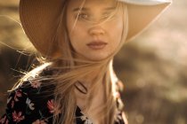 Ritratto di una bella giovane donna con cappello in campagna guardando la macchina fotografica — Foto stock