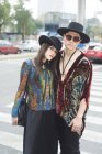 Couple élégant confiant en vêtements hipster debout embrassant dans la rue en été et regardant la caméra — Photo de stock