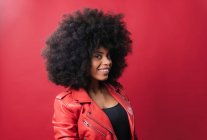 Délicieuse femme afro-américaine avec coiffure afro regardant la caméra sur fond rouge en studio — Photo de stock