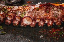 Delicious grilled octopus tentacle served with spices on wooden board — Stock Photo