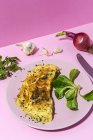 Omelete saborosa na placa contra raminhos de salsa frescos e cebola vermelha com dentes de alho no fundo rosa — Fotografia de Stock