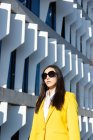 Asiatische Geschäftsfrau mit gelbem Mantel läuft die Straße hinunter, im Hintergrund ein Gebäude — Stockfoto