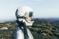 Вид сбоку мужчины-астронавта в скафандре и шлеме, стоящего на траве и камнях в высокогорье — стоковое фото